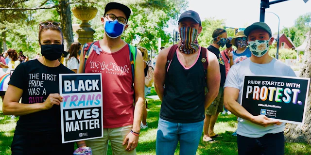 Four people standing outside in masks and holding up a sign that says Black Trans Lives Matter