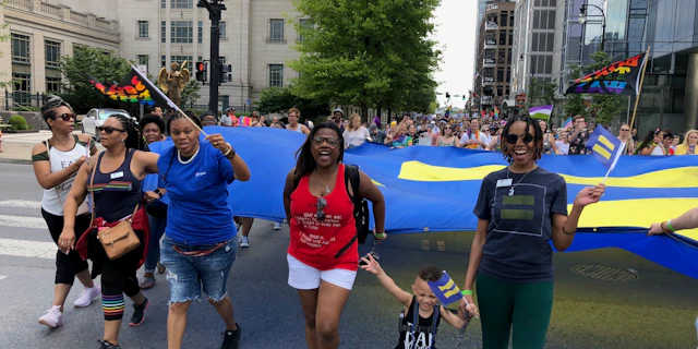 Group of people walking the in the middle of the street in a protest formation, holding HRC flags