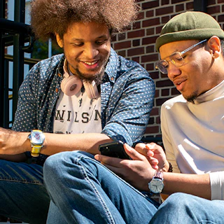 Two Black men sitting outside on a stoop looking at a cell phone.